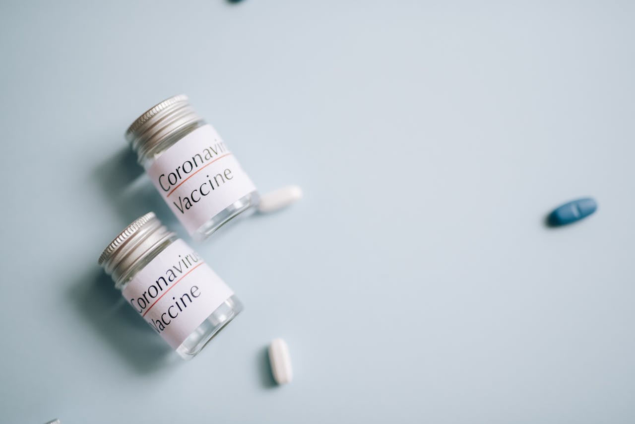 Close-up of coronavirus vaccine vials with scattered pills on a blue background, symbolizing healthcare efforts.
